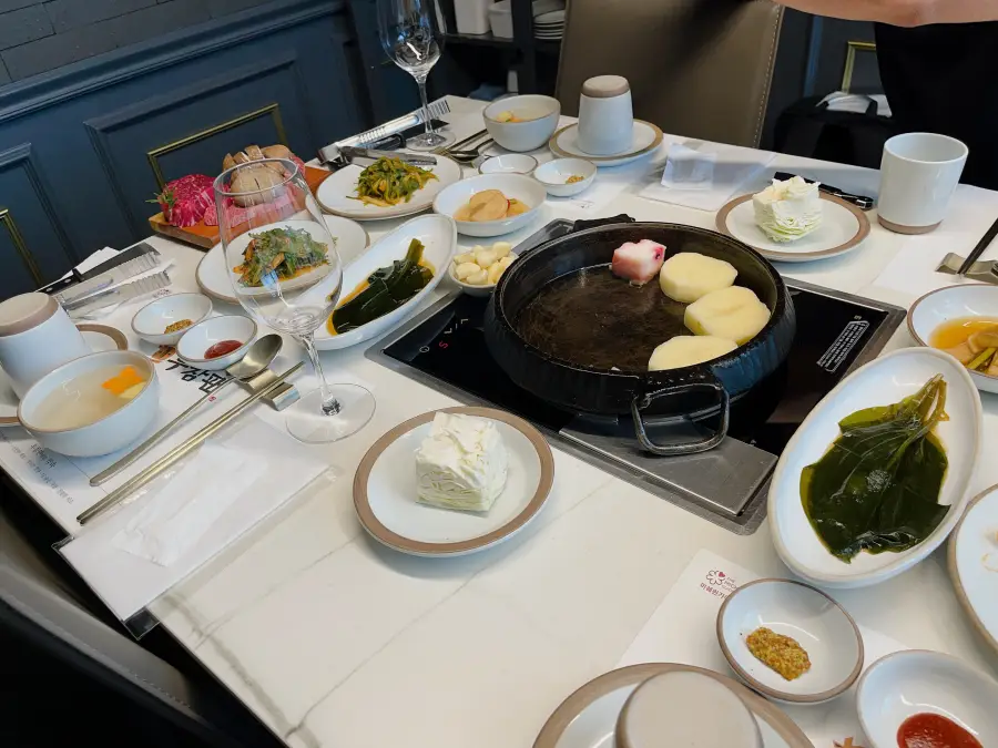 Tavola del ristorante apparecchiata con una padella in ghisa con patate e vari contorni (banchan)