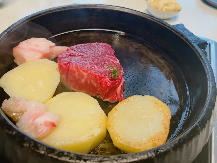 Un grosso pezzo di carne di manzo in cottura su una padella in ghisa insieme a fette di patate e grasso di manzo