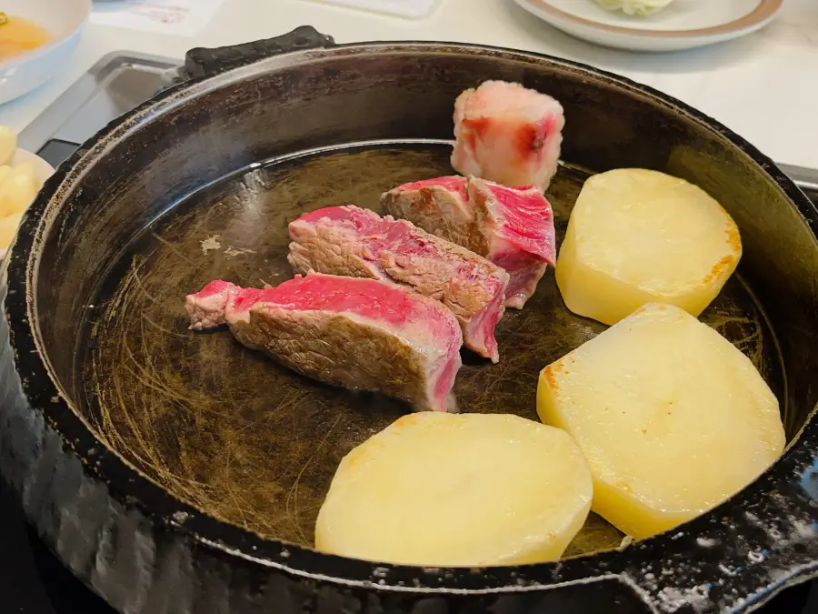 Carne di manzo rosolata all'esterno tagliata in più pezzi e disposta su una padella in ghisa con patate