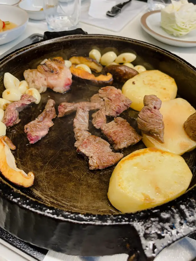 Carne di manzo, aglio, funghi e patate in cottura su una padella in ghisa nera