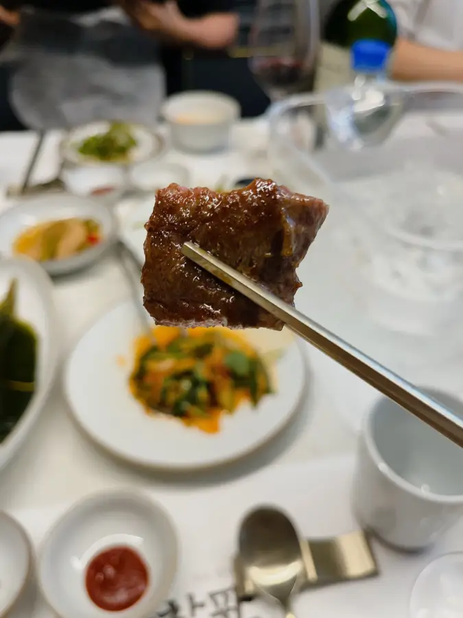 Un pezzo di carne di manzo ben grigliata sollevato con le bacchette e contorni sulla tavola