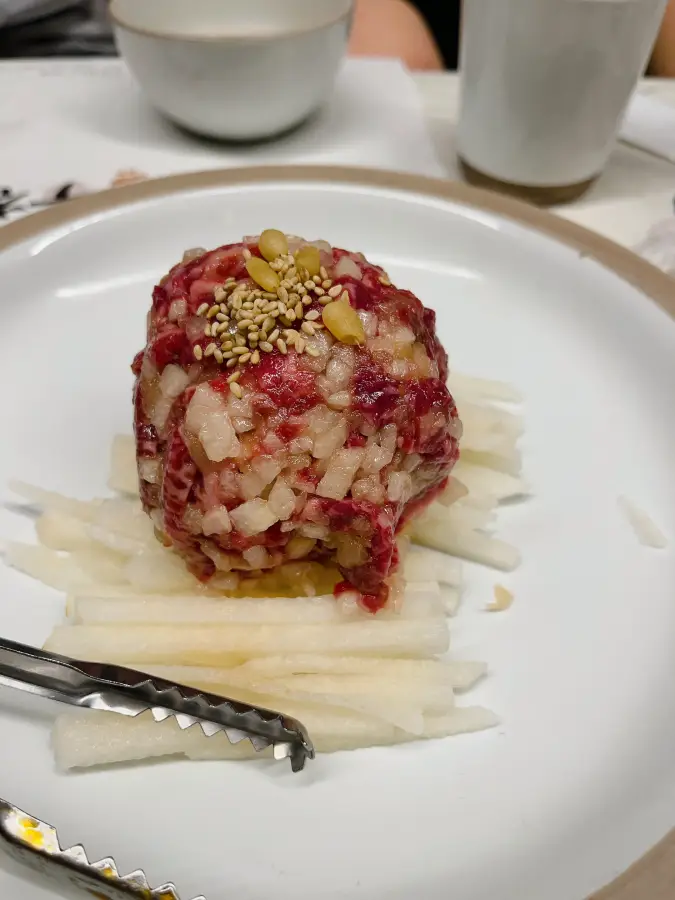 Yukhoe (tartare di manzo) a forma di palla su pere tagliate a julienne, cosparsa di pinoli e semi di sesamo