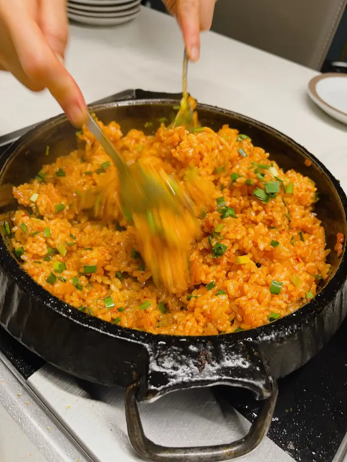Kkakdugi bokkeumbap (riso fritto con kimchi) in una padella in ghisa nera mescolato con due cucchiai